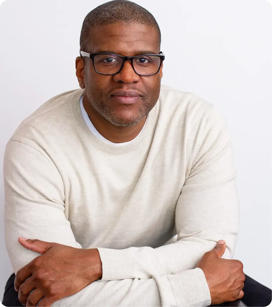 Man wearing glasses and a light beige sweater with arms crossed.