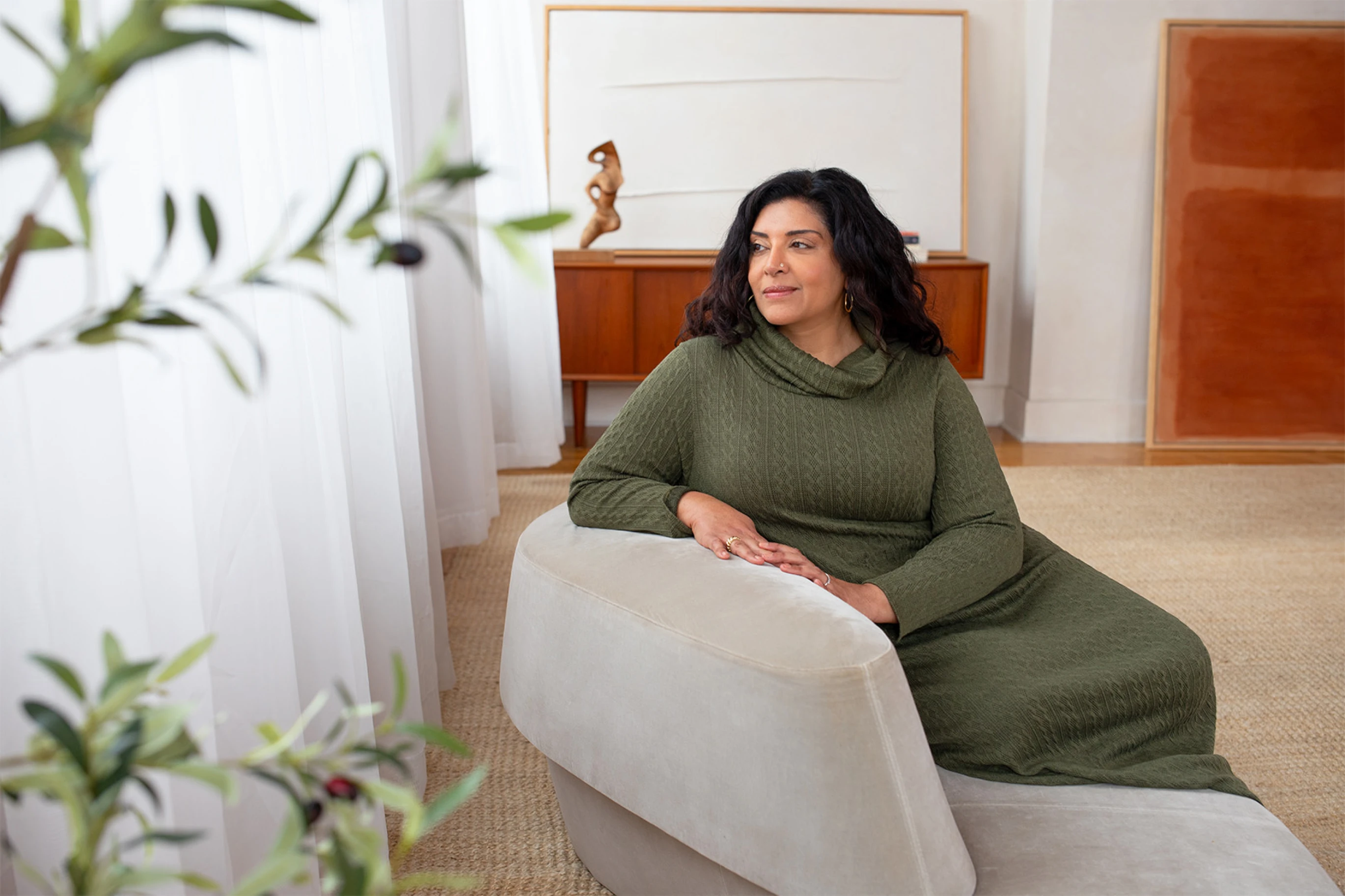 Harjeet Badwall seated on a sofa arm, looking out a window