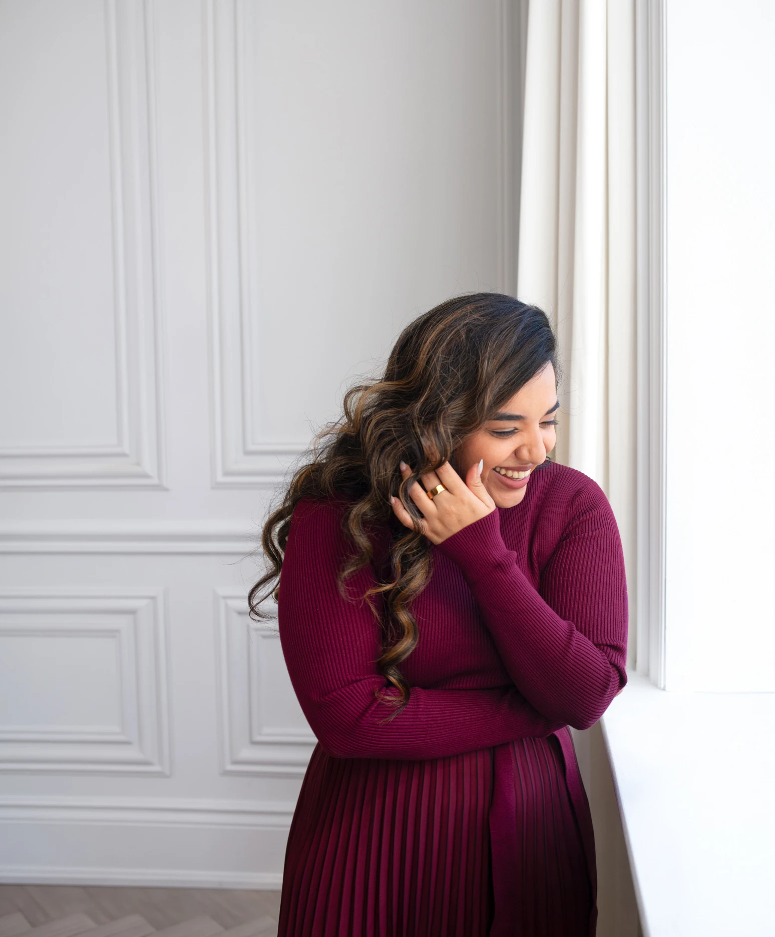 A therapist in a burgundy sweater laughing beside a window